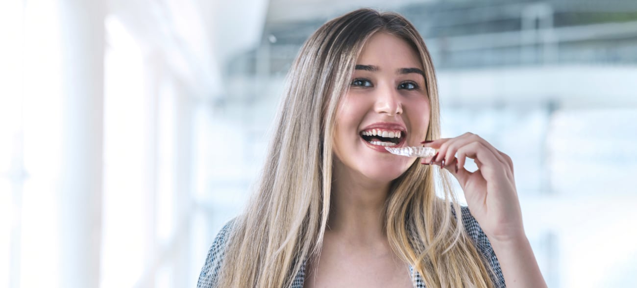 Une jeune femme blonde met en place une gouttière Invisalign.