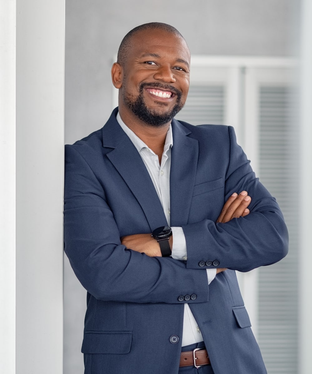 Un homme vêtu d'une chemise bleue boutonnée et d'un veston marche dans la rue en souriant.